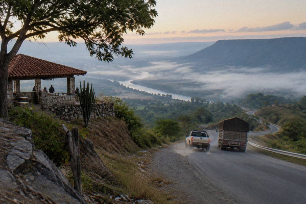 Highway curving between forested mountains with mist over the valley