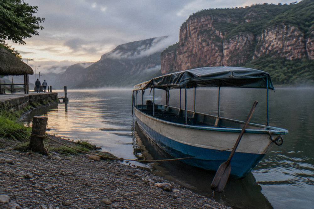 A covered speedboat moored at a riverside dock with canyon cliffs behind it