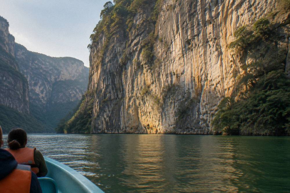 Sunlight striking the face of a tall limestone cliff above a calm green river