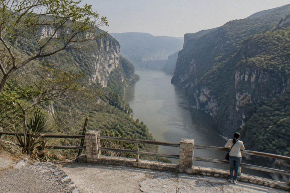 A wide view down a reservoir between forested canyon walls toward a distant dam