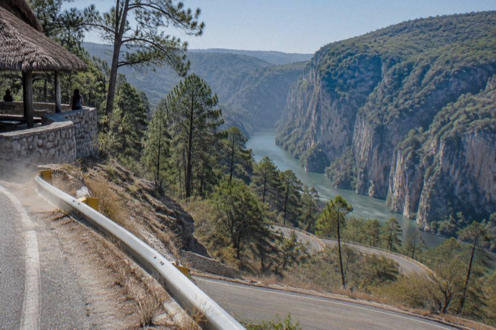 Winding mountain highway descending through pine forest toward a wide river valley