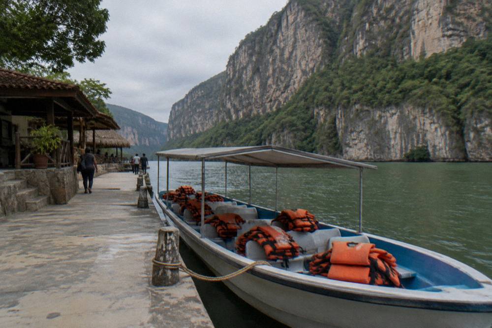 Shared tour boat moored at a river dock beside tall canyon walls