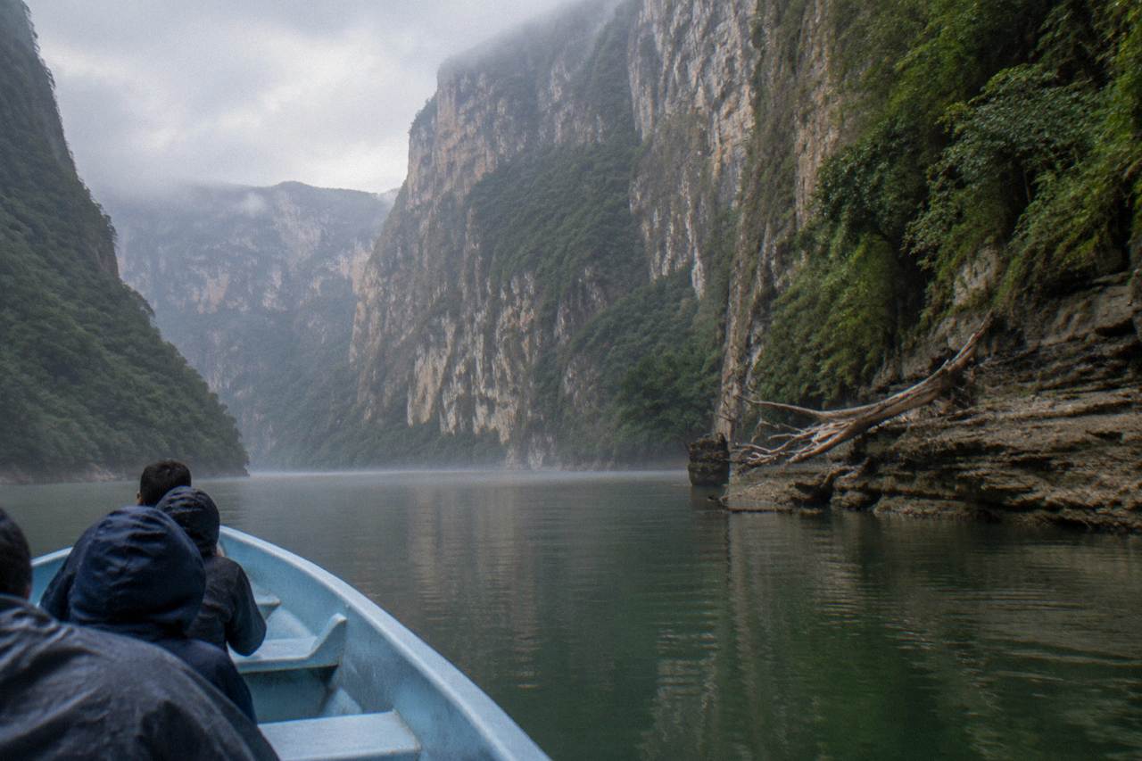 A boat crossing calm green water toward tall canyon walls in Chiapas