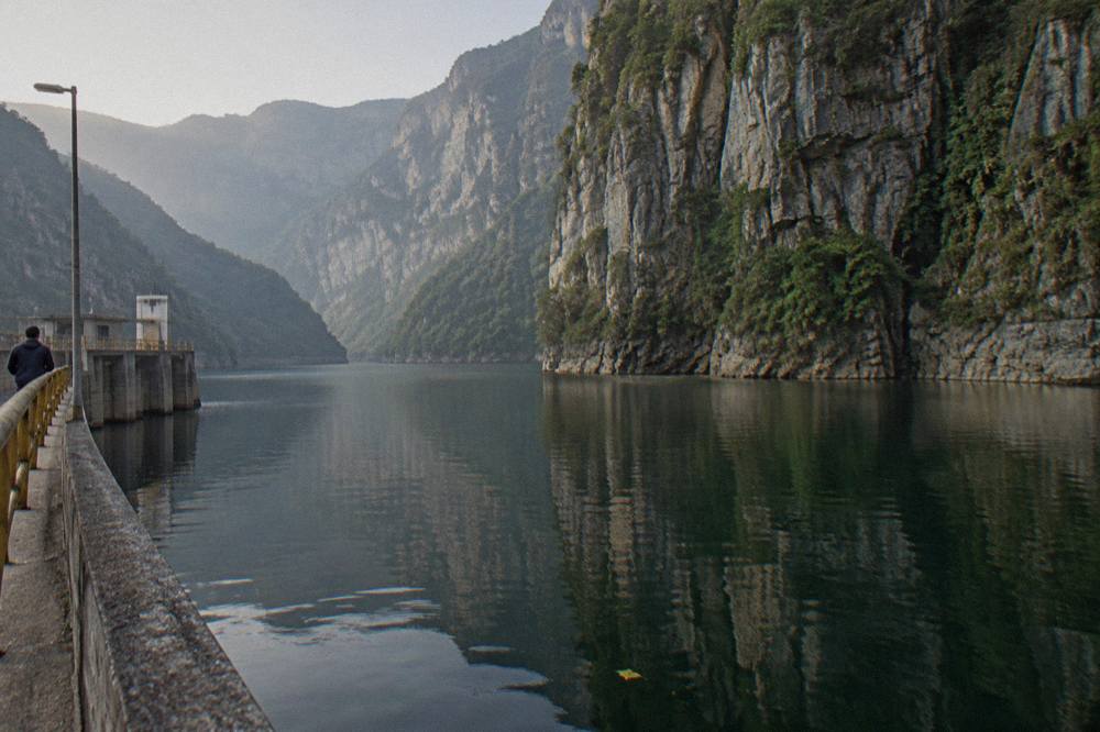 Layered limestone cliff face rising steeply from calm green water with vegetation clinging to the rock
