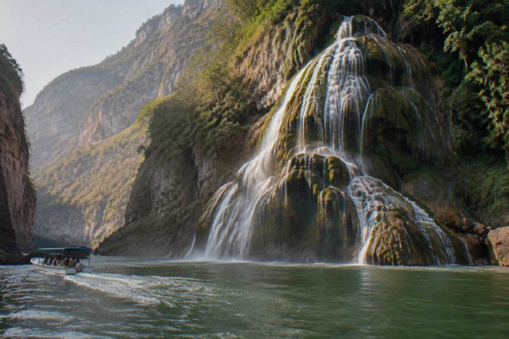 Tall waterfalls pouring down a green cliff face into a turquoise pool surrounded by forest