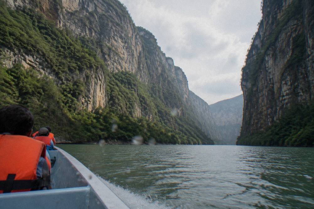 A small boat traveling on a wide river between towering sheer canyon walls