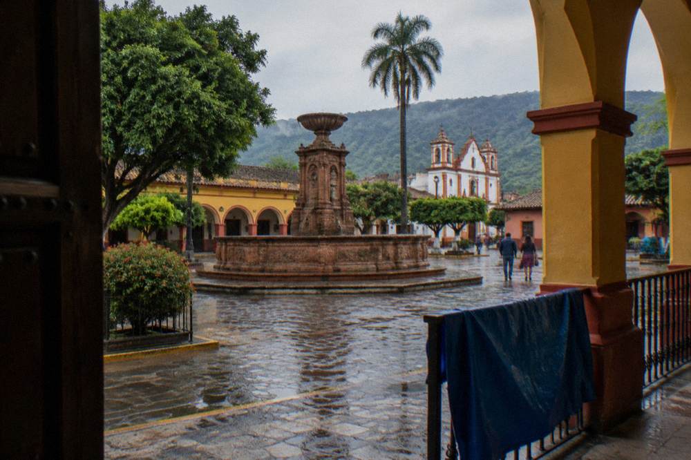 Colorful colonial buildings and a brick fountain in a small town plaza near a river
