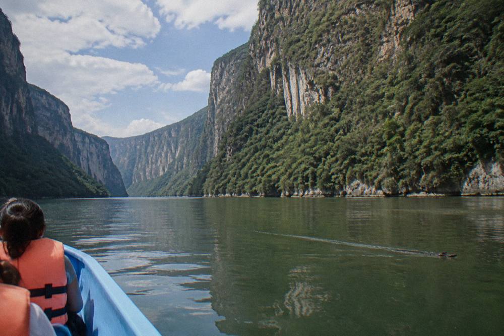 A wide river bend between steep forested canyon walls under a partly cloudy sky