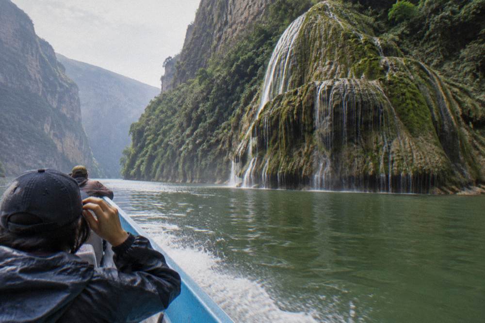 Long-tail boat crossing wide green water between towering canyon cliffs