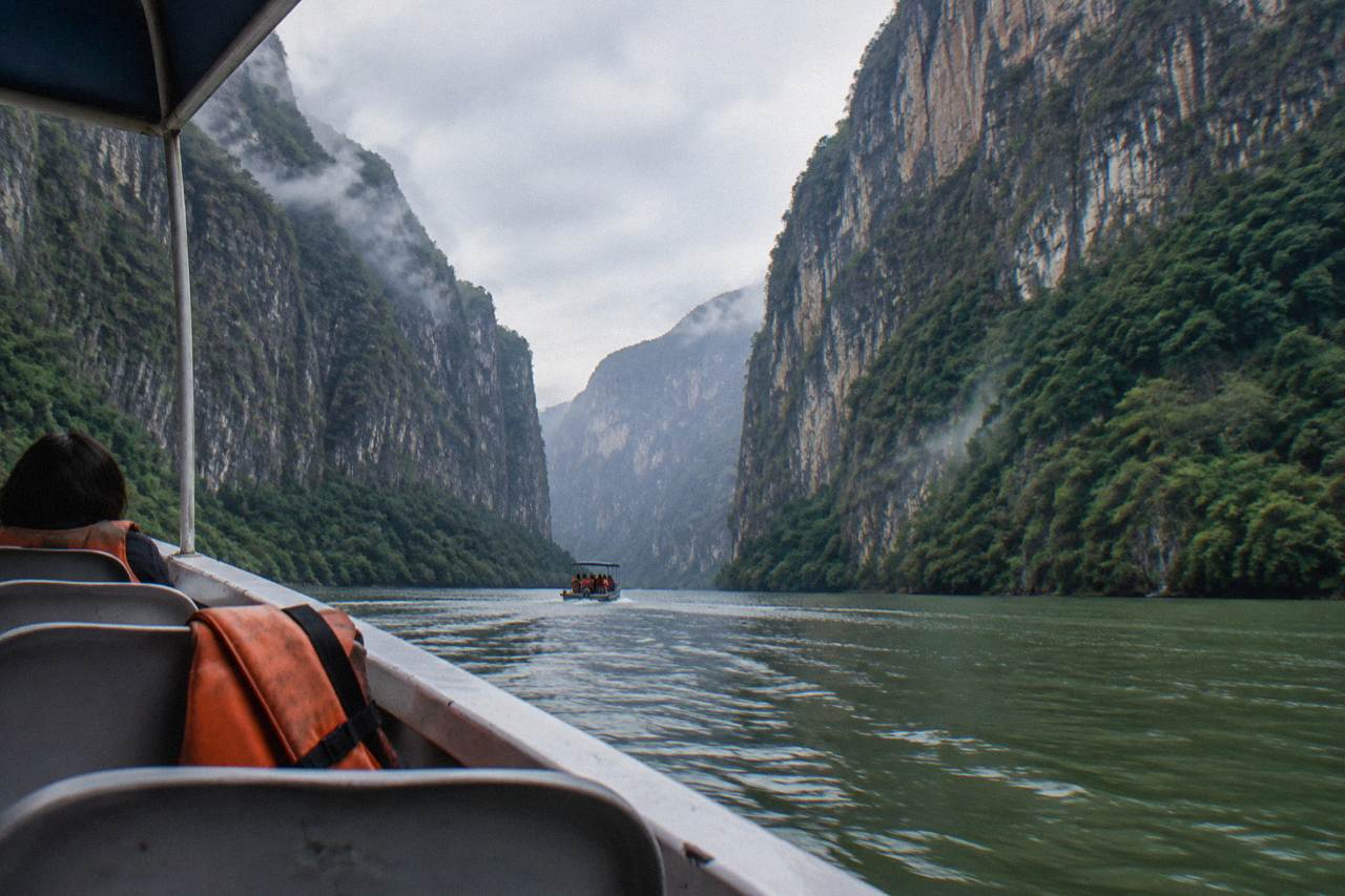 Tall limestone cliffs rising above a wide green river inside a deep canyon
