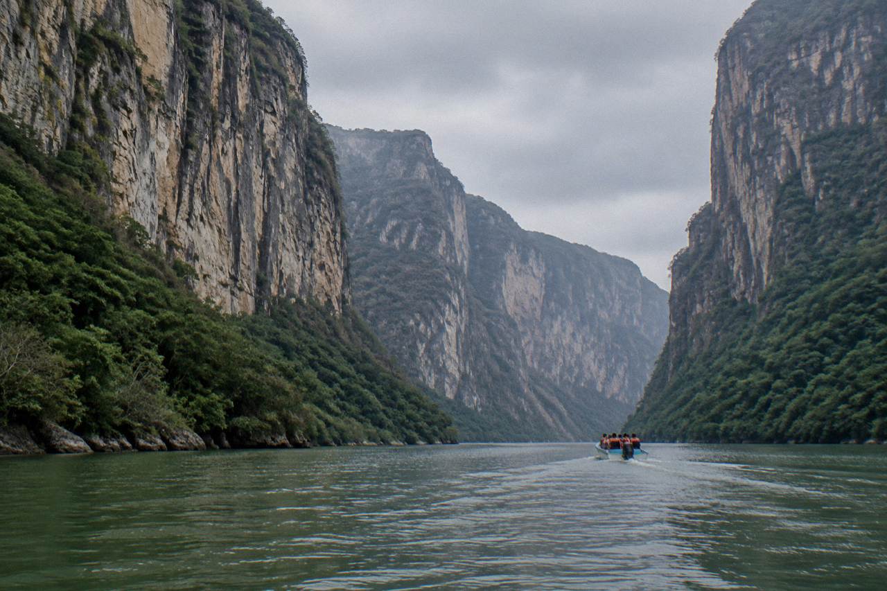High limestone walls of Sumidero Canyon rising above the green Grijalva River under a cloudy sky
