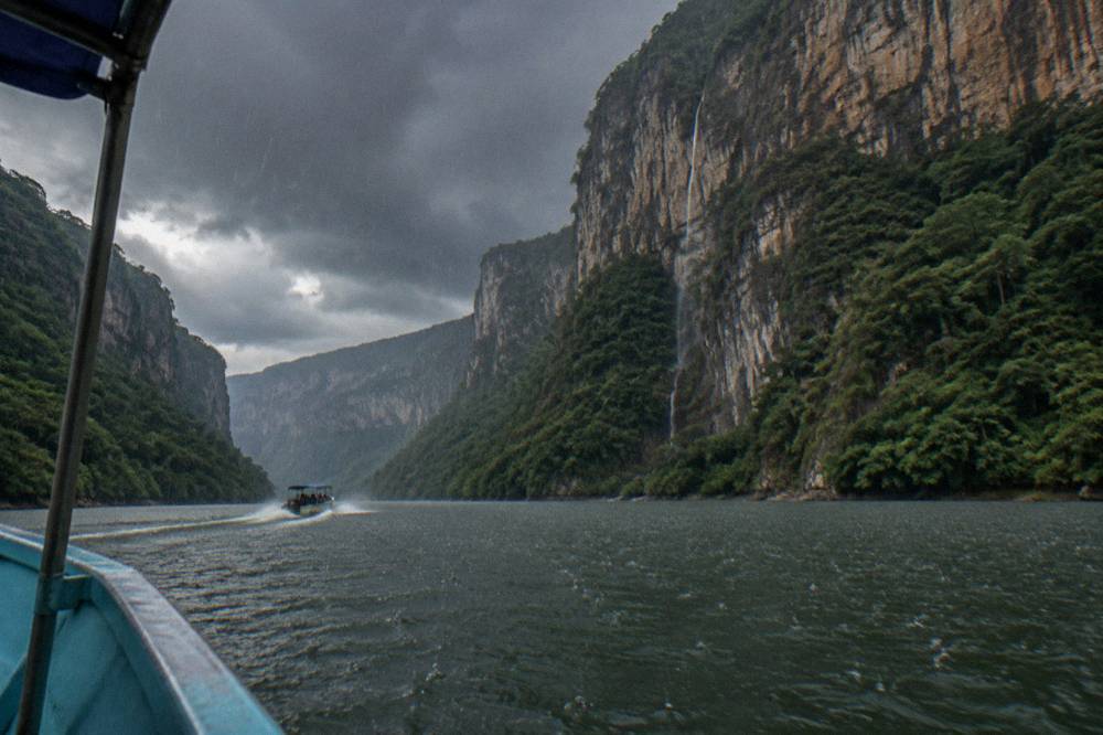 Dark rain clouds gathering above green canyon walls with water streaking down the rock face