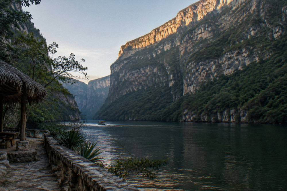 Sunlight striking the upper edge of a high rock cliff above a calm river bend