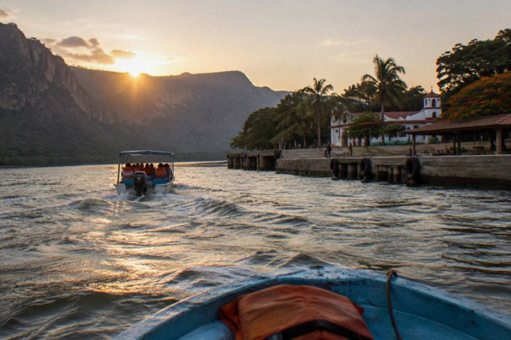 Tourist boat returning along a wide river toward docks as the sun lowers over cliffs