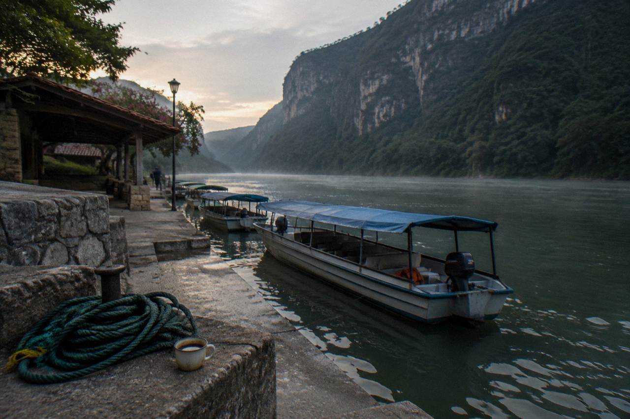 Small covered boats moored at a river dock below tall canyon cliffs in early daylight