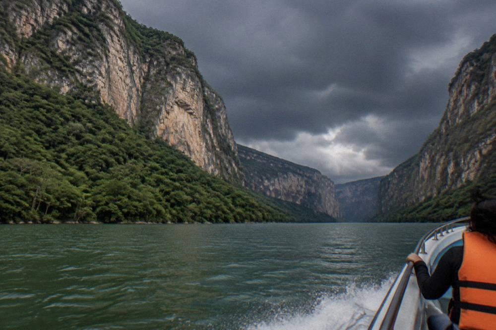 Dramatic rain clouds gathering over steep forested canyon walls above a calm river