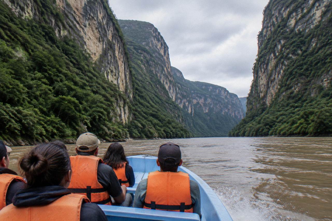 Speedboat on a wide river between tall forested canyon walls under an overcast sky