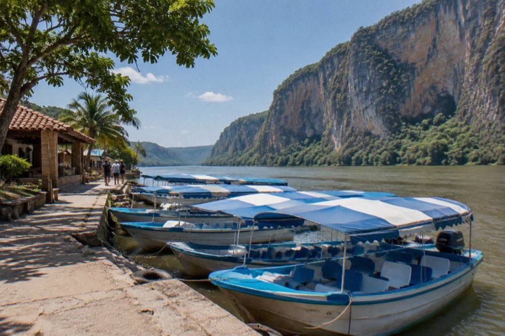 Covered tourist boats tied at a riverside dock with a cliff wall rising behind them