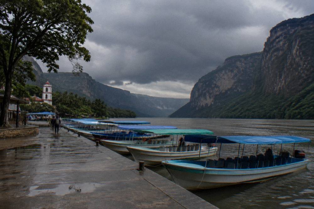 A line of shared tour boats with canopy roofs waiting at a dock on a wide river
