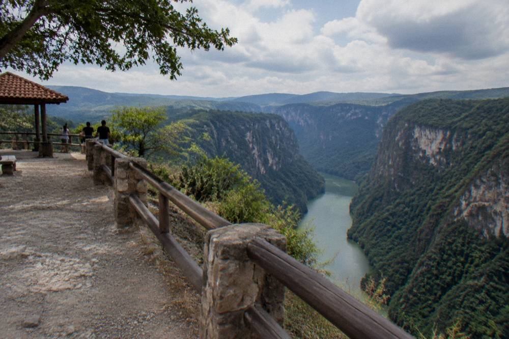 A wide river winding between tall forested canyon walls under a partly cloudy sky