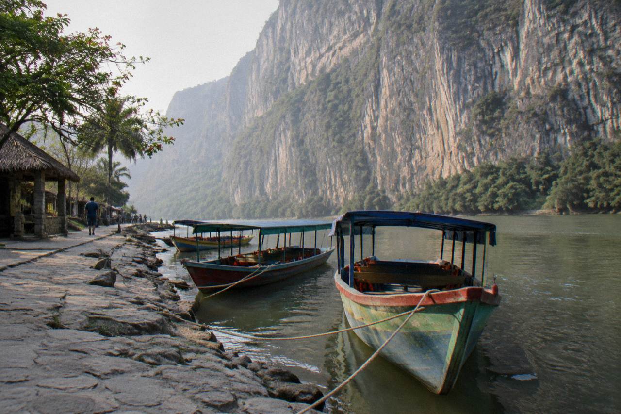 Wooden boats moored along the Grijalva River at a Sumidero Canyon embarcadero with cliffs behind
