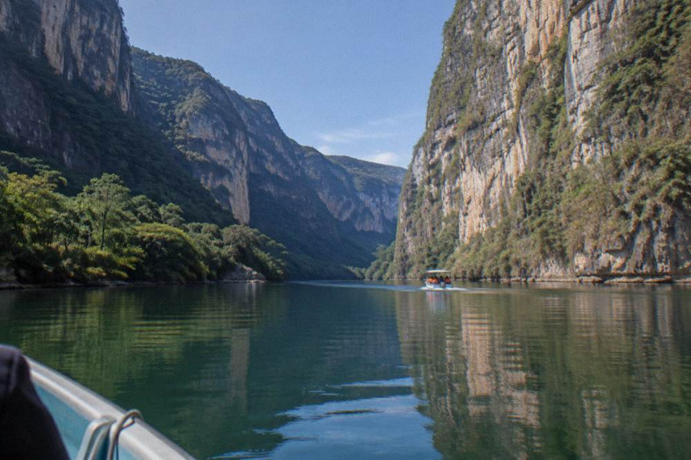 Clear dry-season sky above the calm green river between the canyon cliffs