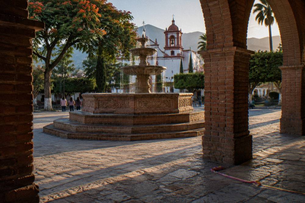Colonial arcade and fountain in a small Mexican town plaza in late afternoon light