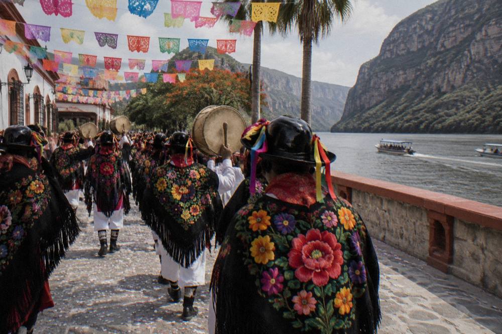 Masked Parachico dancers in embroidered shawls moving through a decorated street