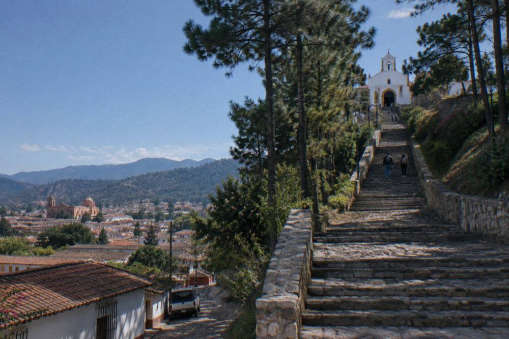 Sunlit central plaza in San Cristobal with benches, trees and colonial arcades