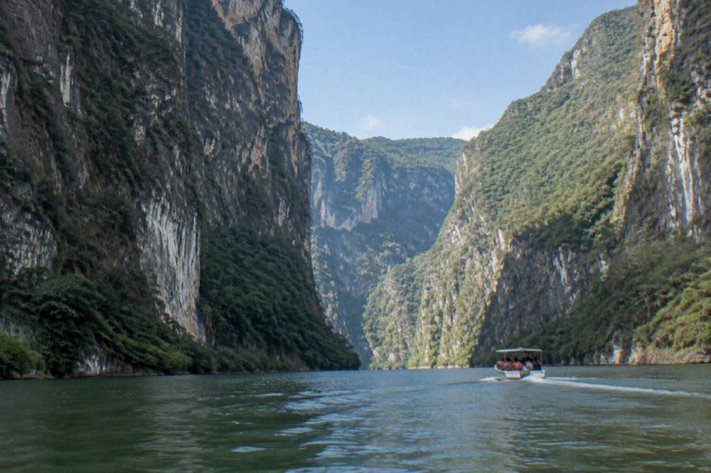 Boat passing between tall canyon walls on a wide river