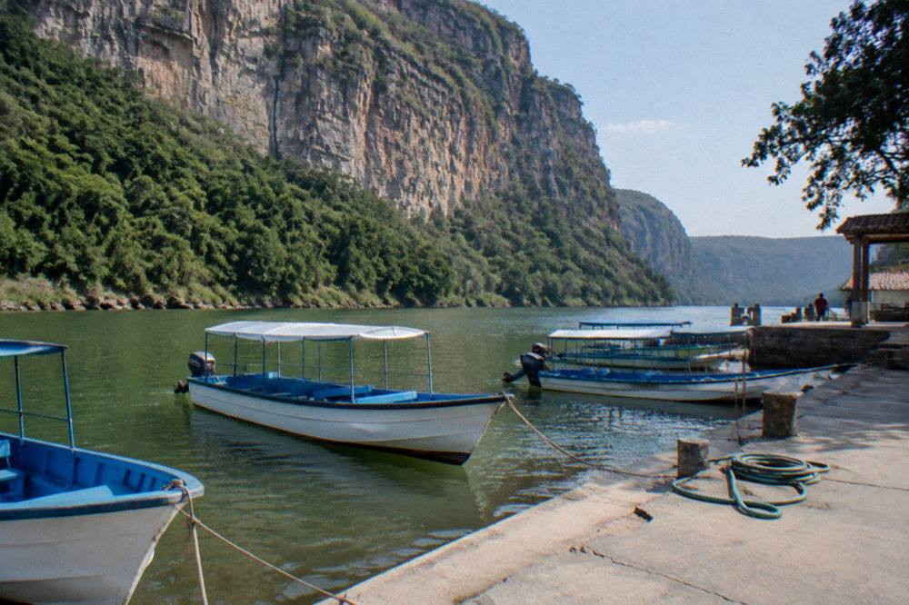 Small boats moored at a riverside dock with a cliff rising behind them