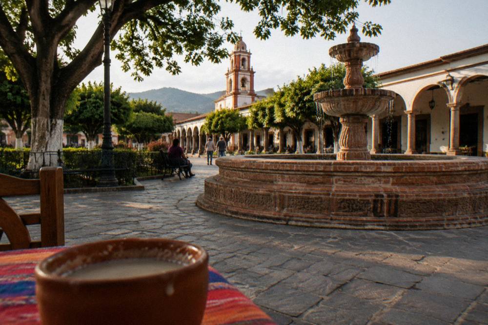 A colonial plaza with a tall brick fountain and arcades in late afternoon light