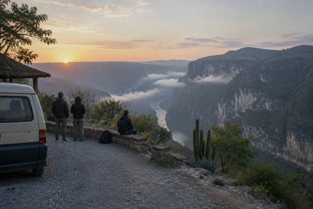 A parked van and travelers at a roadside overlook above a deep river gorge