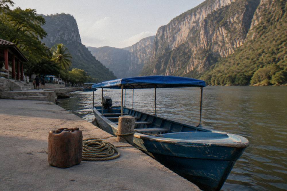A covered motorboat moored at a river dock with canyon walls in the background