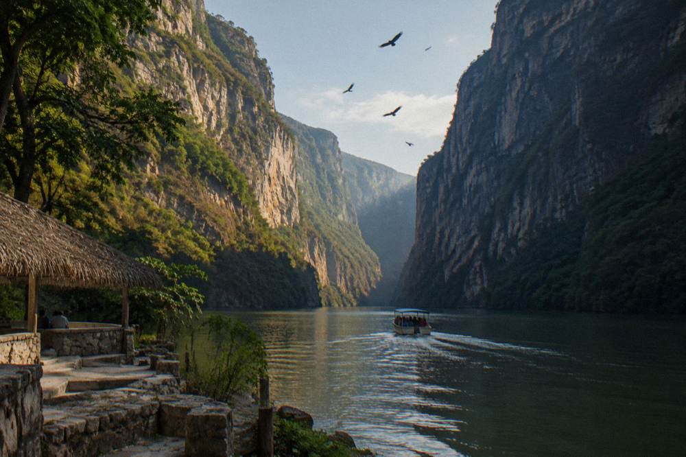 Sheer limestone canyon walls rising above green water with morning shadow on one face