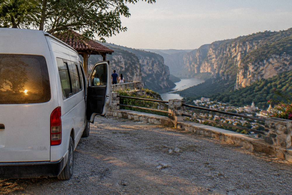 A tour van parked at a roadside viewpoint above a deep river canyon