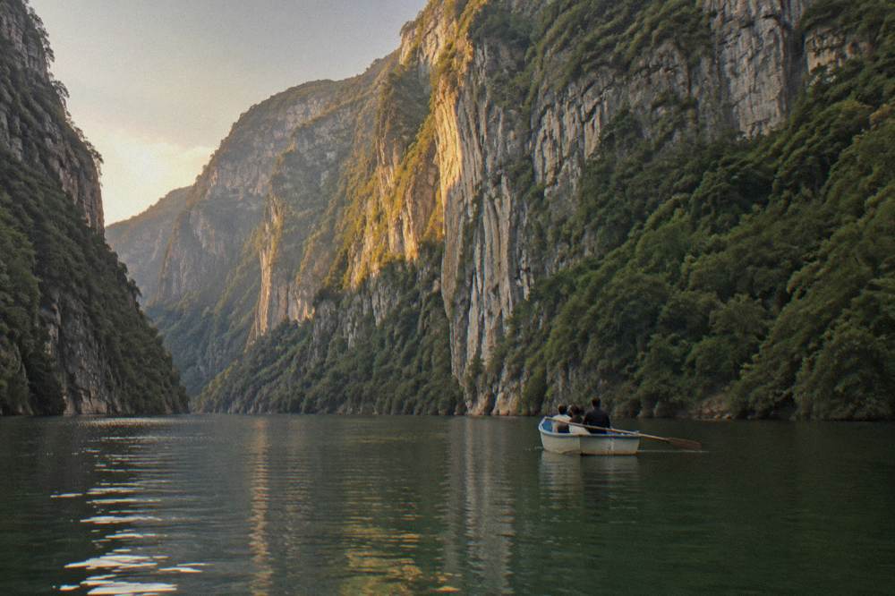 A single small boat on calm water beneath high forested cliffs in late light