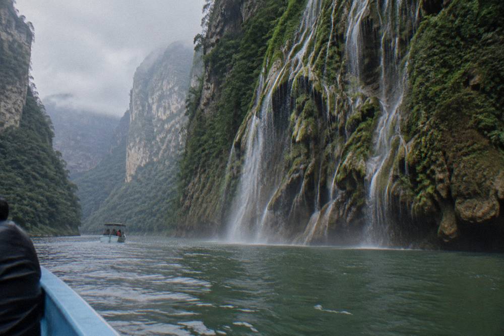 A waterfall clinging to a tall rock face shaped like a tree beside the river