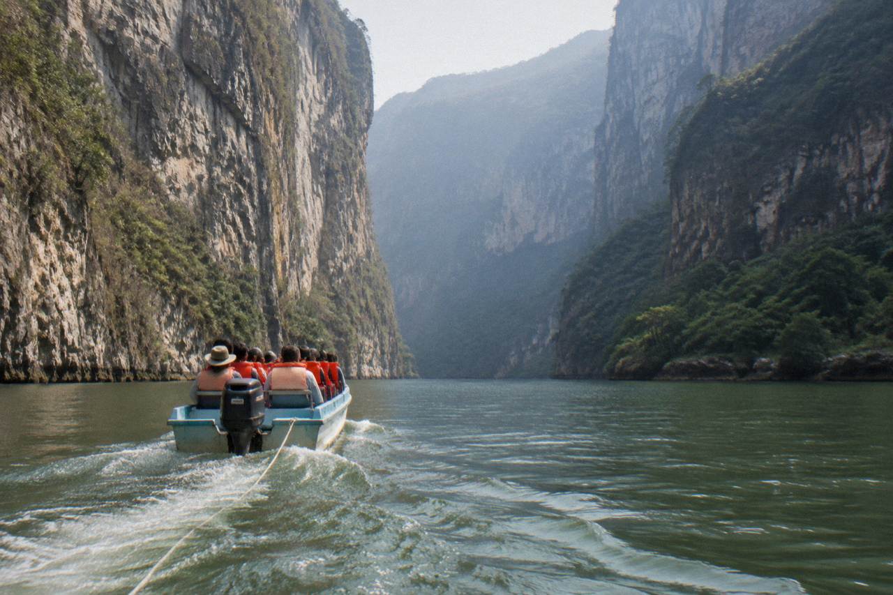 A long shared boat cruising between towering limestone canyon walls on a wide green river