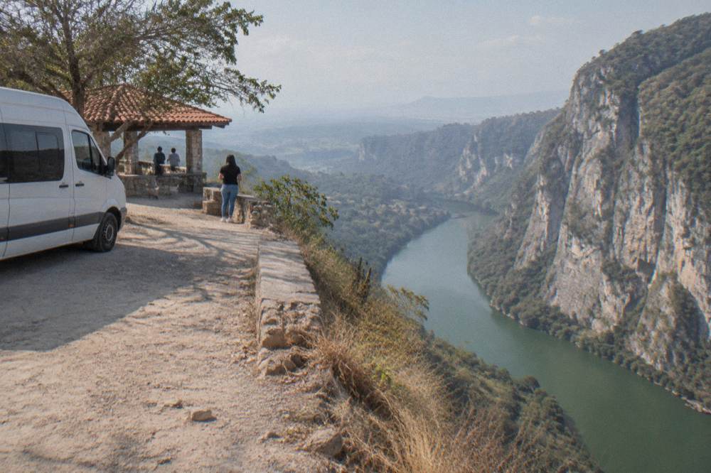 Air conditioned passenger van parked on a roadside viewpoint above a wide river canyon
