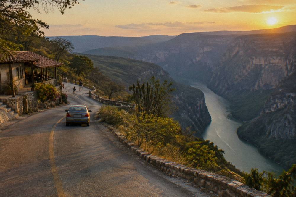 Small sedan on a winding mountain road above forested hills at golden hour