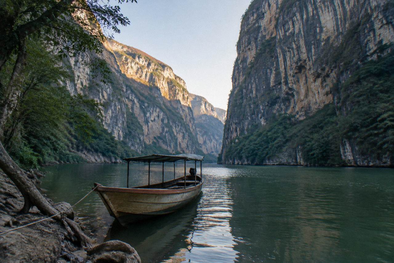 Wooden boat on calm green river between tall limestone canyon walls