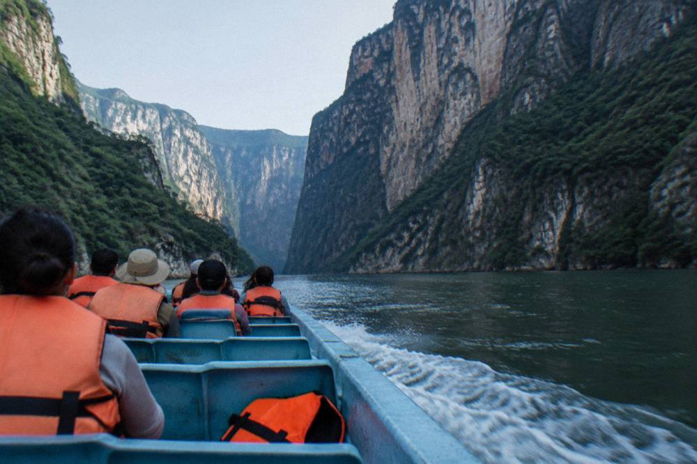 Passengers in life jackets seated in a covered boat departing a river jetty