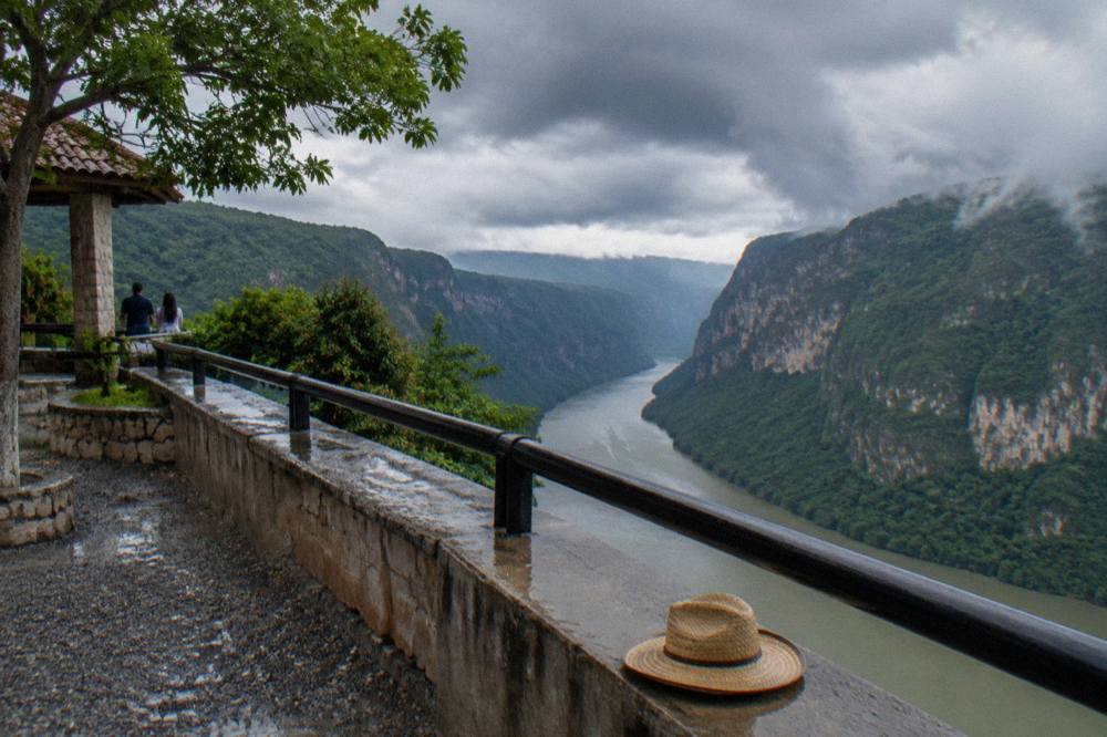 Dark storm clouds building over jungle covered canyon walls above a wide brown river