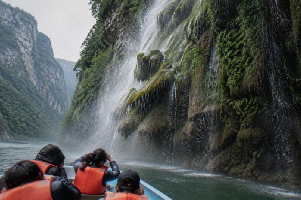 A tall waterfall running down a moss covered rock face inside a steep canyon