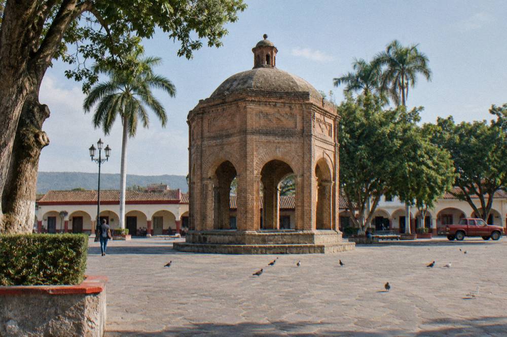 Colonial town square with a brick fountain and colorful facades under afternoon light