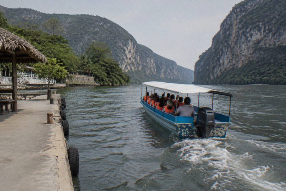Long-tail boat on the Grijalva River passing tall limestone canyon walls in morning light
