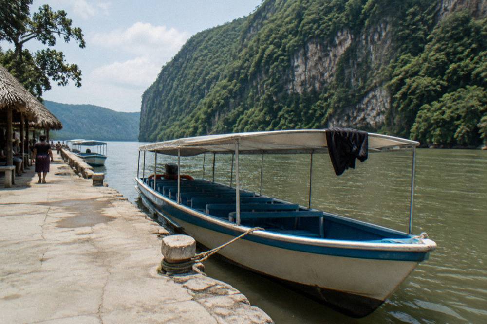 Shared tour boat moored at a wooden dock on the Grijalva River below steep canyon walls