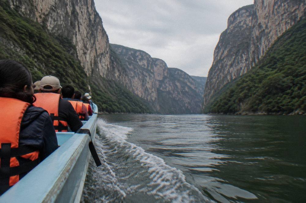 Long open boat carrying passengers along a calm river beneath steep cliff walls