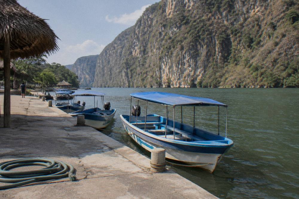 Tourist boats moored at a riverside dock with canyon walls rising behind them